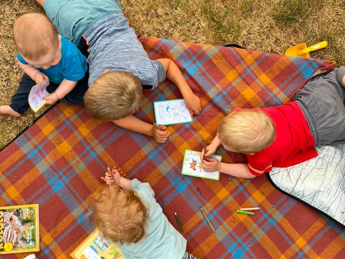 Vier Kinder sitzen und liegen auf einer karierten Decke im Gras und malen mit Buntstiften in kleinen Malbüchern. | © DAV Markt Schwaben / Lara Wolff