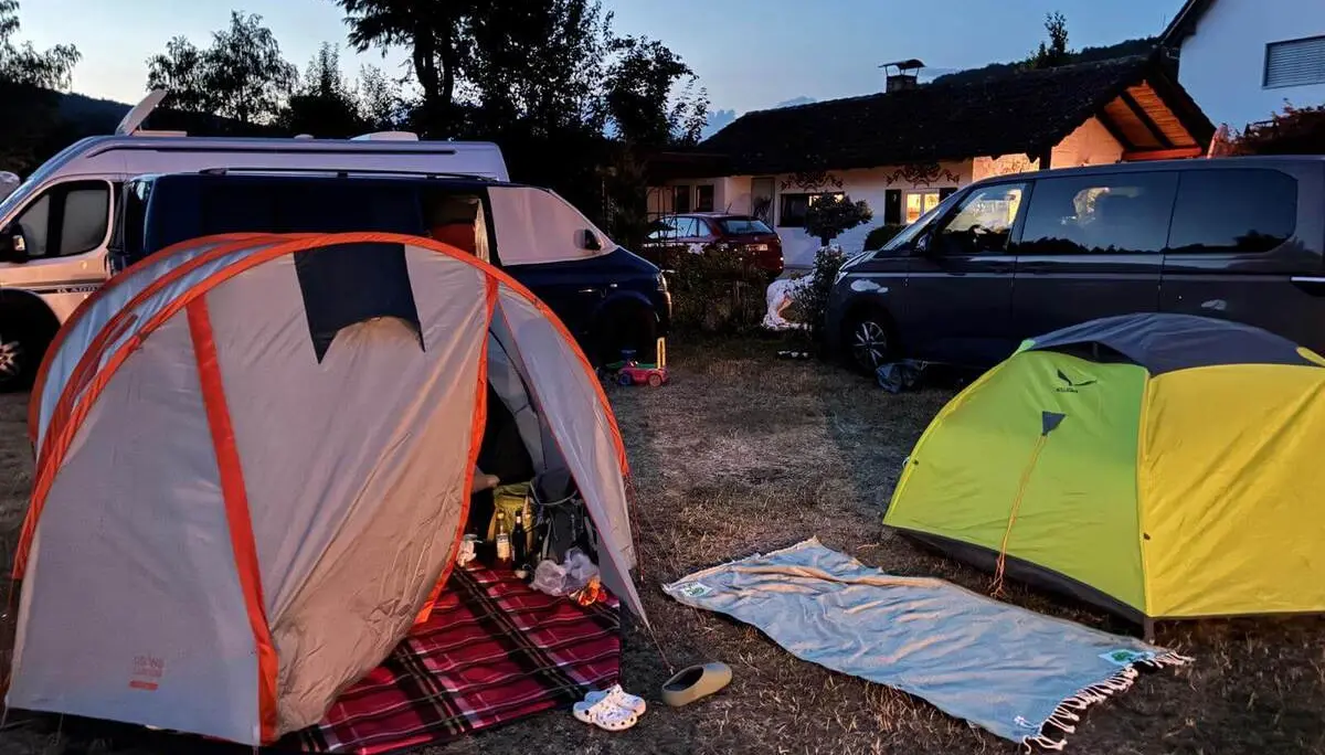 Zwei Zelte stehen zwischen Campingbussen auf einem trockenen Zeltplatz. Die Szene ist in der Abenddämmerung beleuchtet. | © DAV Markt Schwaben / Lara Wolff