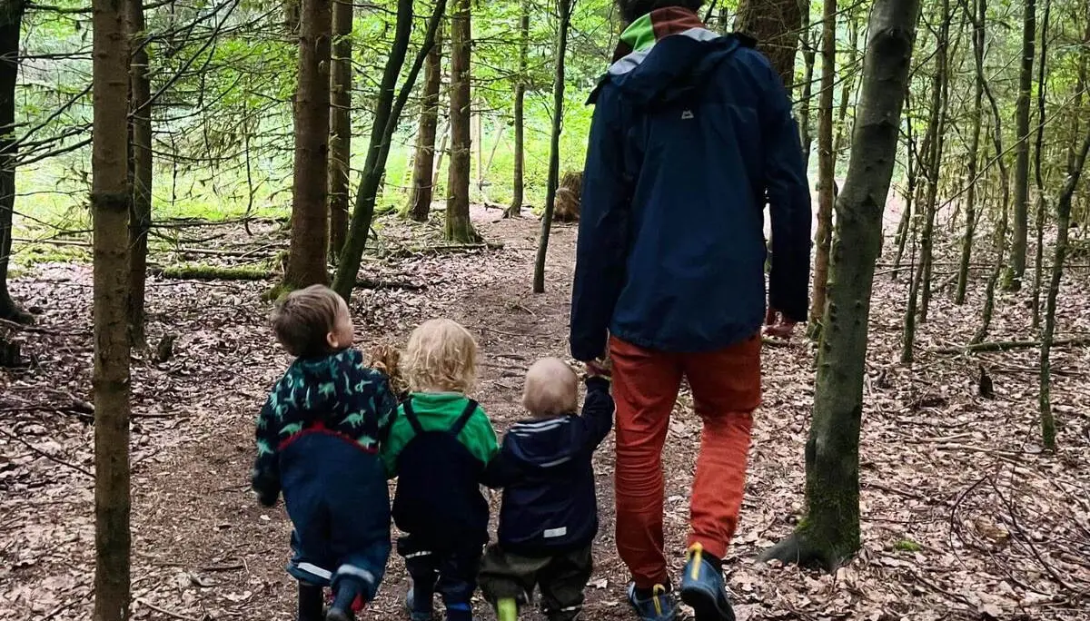 Eine erwachsene Person geht mit drei kleinen Kindern auf einem schmalen Waldweg. Hohe Bäume säumen den Pfad durch den Wald. | © DAV Markt Schwaben / Lara Wolff