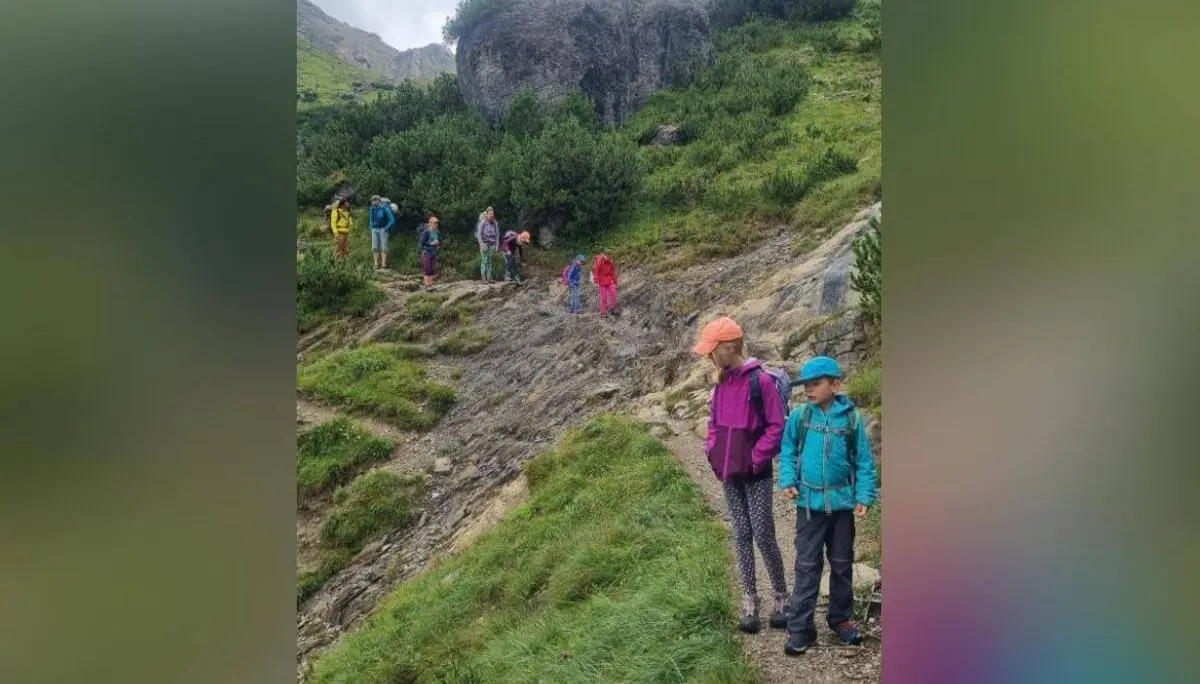 Mehrere Erwachsene und Kinder wandern auf einem schmalen Bergpfad über felsiges Gelände mit Grüngras und Felsen im Hintergrund. | © DAV Markt Schwaben / Silke Titze