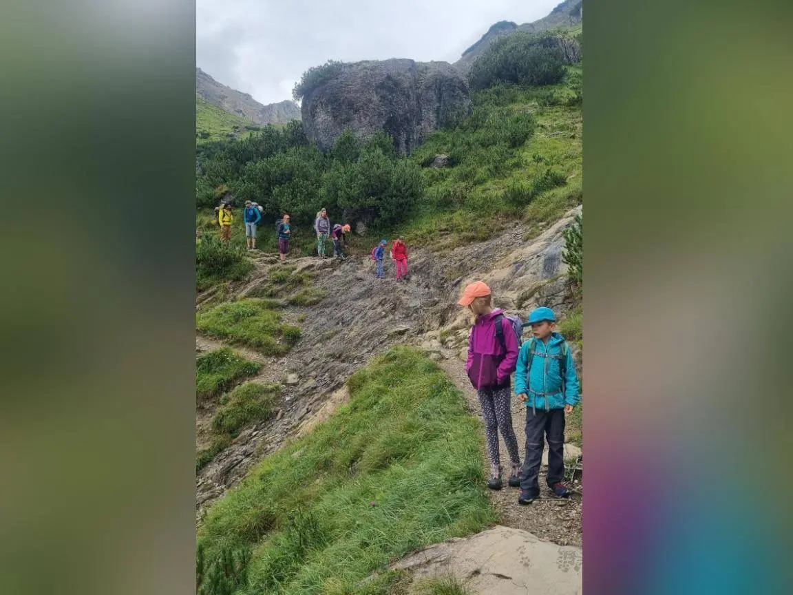 Mehrere Erwachsene und Kinder wandern auf einem schmalen Bergpfad über felsiges Gelände mit Grüngras und Felsen im Hintergrund. | © DAV Markt Schwaben / Silke Titze
