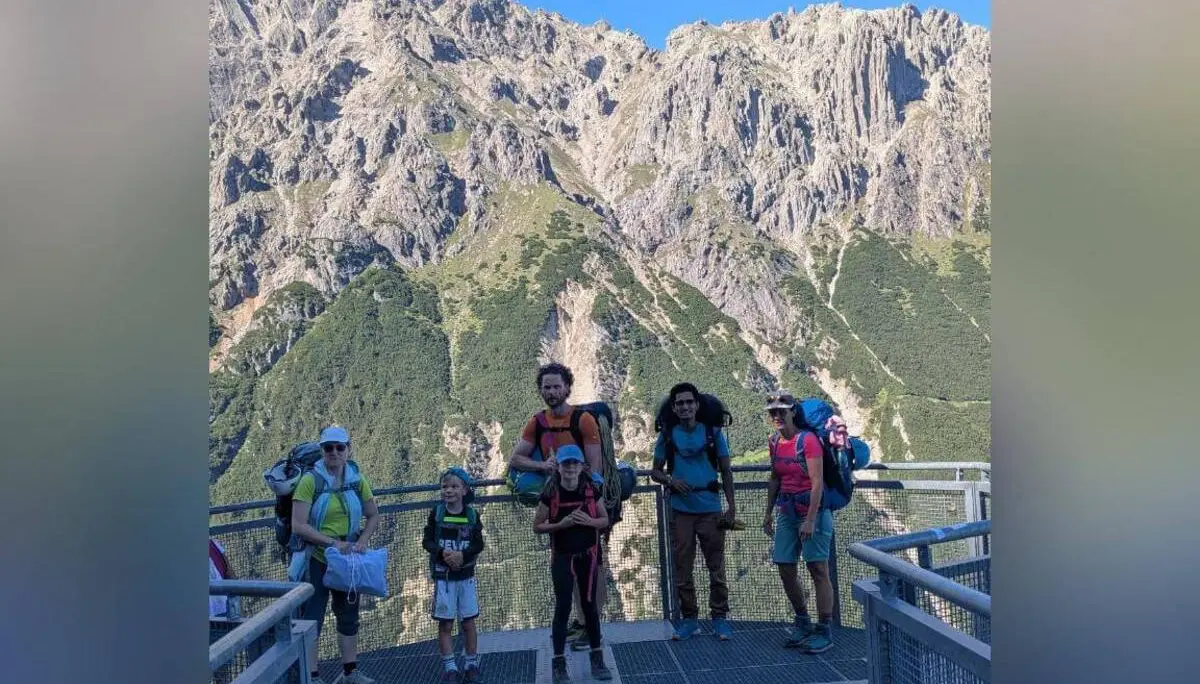 Fünf Wandernde mit Rucksäcken stehen auf einer Aussichtsplattform an der Bergstation. Dahinter ragen steile Felswände vor blauem Himmel auf. | © DAV Markt Schwaben / Silke Titze