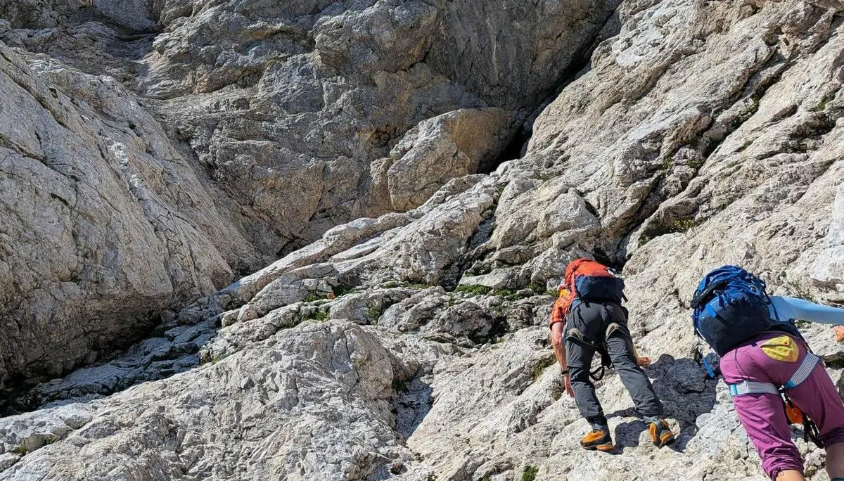 Zwei Personen mit Rucksäcken steigen über steile Kalkfelsen auf. Das helle, schrofige Gelände erfordert den Einsatz von Händen und Füßen. | © DAV Markt Schwaben/Michael Huber