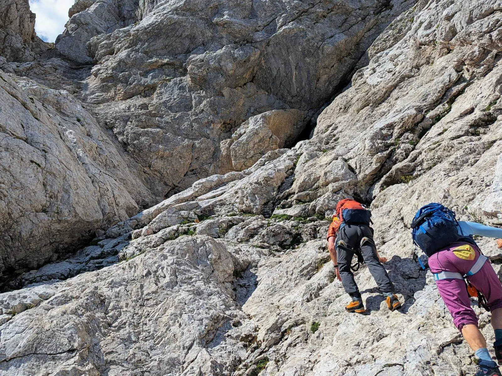 Zwei Personen mit Rucksäcken steigen über steile Kalkfelsen auf. Das helle, schrofige Gelände erfordert den Einsatz von Händen und Füßen. | © DAV Markt Schwaben/Michael Huber