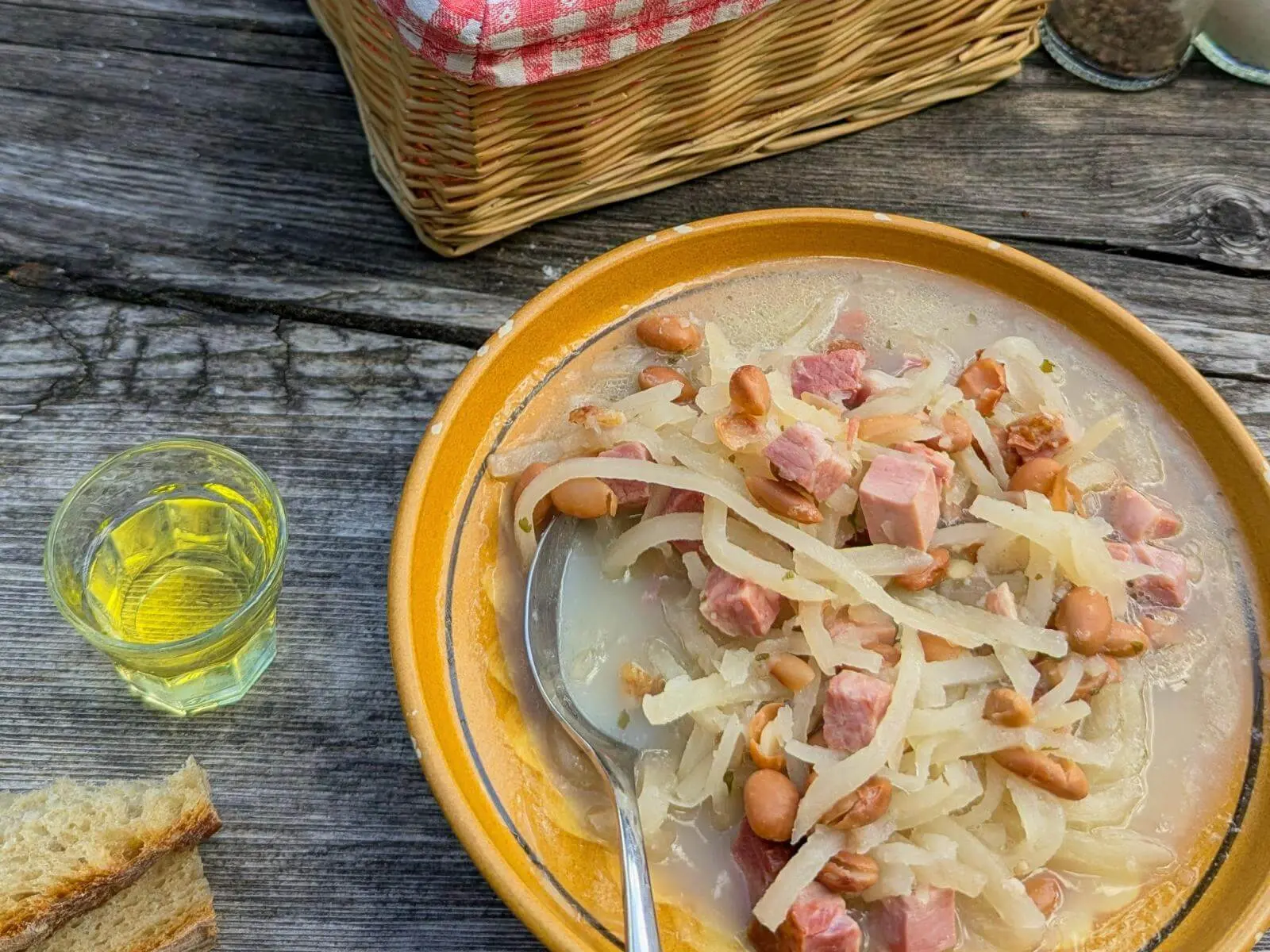 Eine Schüssel Jota mit Bohnen, Sauerkraut und Schinkenwürfeln steht auf einem Holztisch. Daneben liegen Brot und ein kleines Glas Getränk. | © DAV Markt Schwaben/Michael Huber