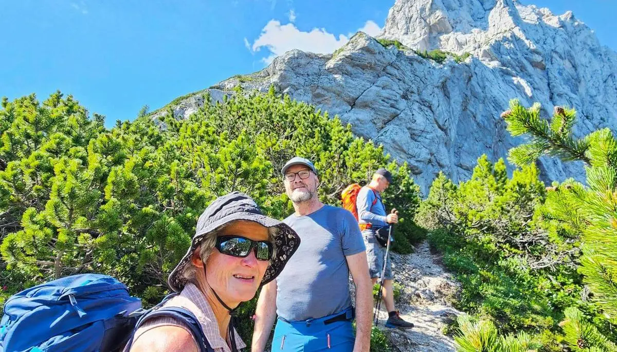 Drei Wandernde stehen auf einem schmalen Bergpfad zwischen Latschenkiefern. Über ihnen ragt eine helle, steile Felswand in den blauen Himmel. | © DAV Markt Schwaben/Lutz Gründel