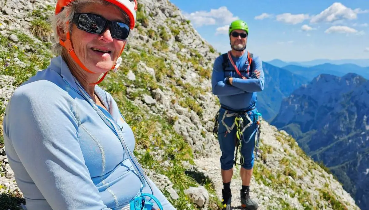 Zwei Personen mit Klettersteigausrüstung halten auf einem schmalen Felsband inne. Im Hintergrund öffnen sich steile Felswände und tiefe Bergtäler. | © DAV Markt Schwaben/Lutz Gründel