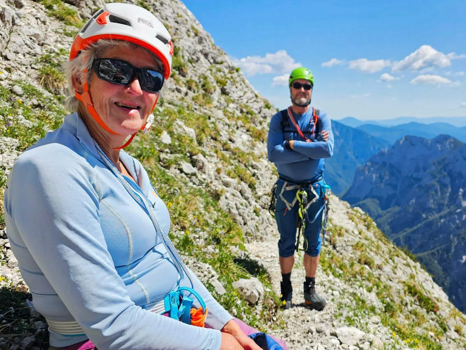 Zwei Personen mit Klettersteigausrüstung halten auf einem schmalen Felsband inne. Im Hintergrund öffnen sich steile Felswände und tiefe Bergtäler. | © DAV Markt Schwaben/Lutz Gründel
