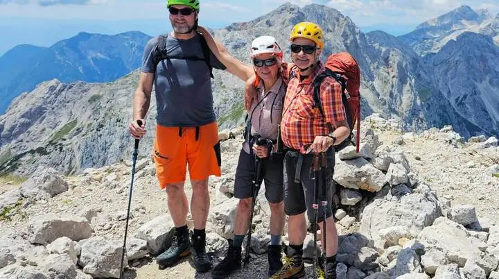 Drei Personen mit Helmen und Wanderstöcken stehen auf dem felsigen Gipfel der Ojstrica. Im Hintergrund erstreckt sich die Bergwelt der Steiner Alpen. | © DAV Markt Schwaben/Lutz Gründel
