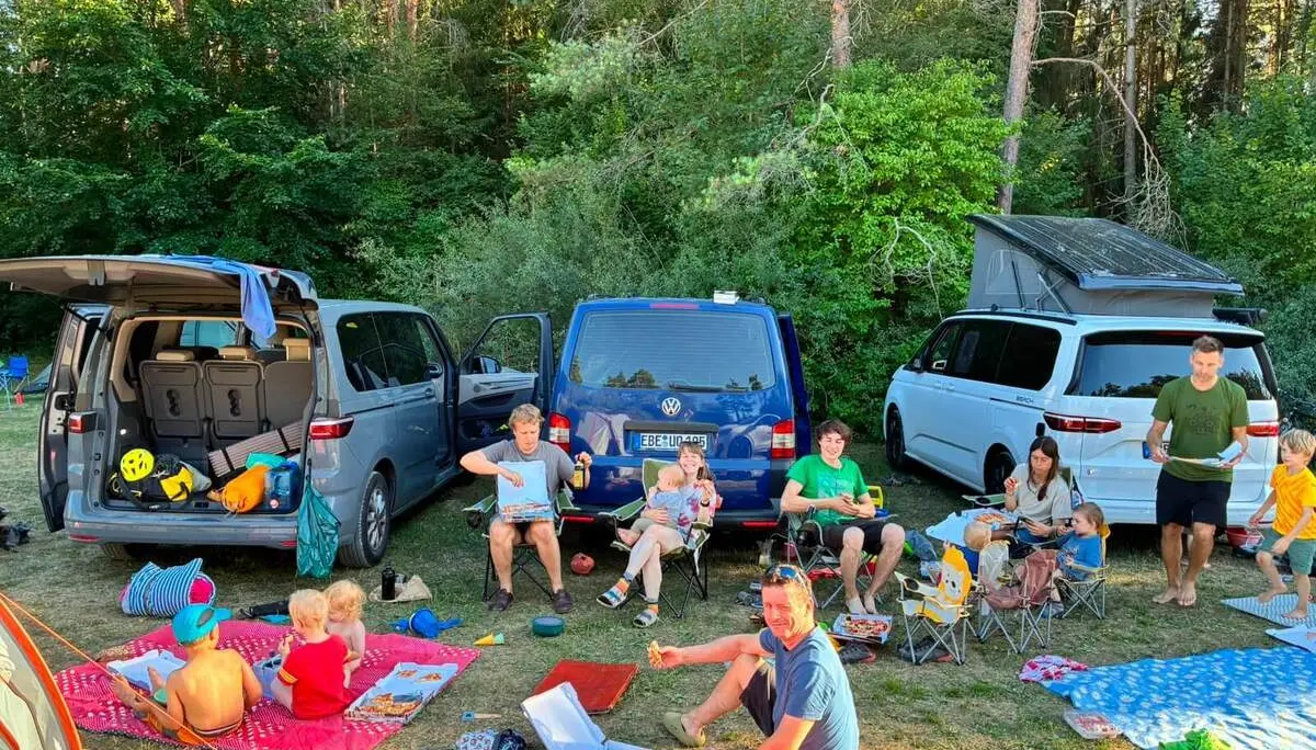 Familien sitzen auf Decken und Campingstühlen zwischen Fahrzeugen und Zelten. Auf dem Platz wird gemeinsam gegessen und pausiert. | © DAV Markt Schwaben/Lara Wolff