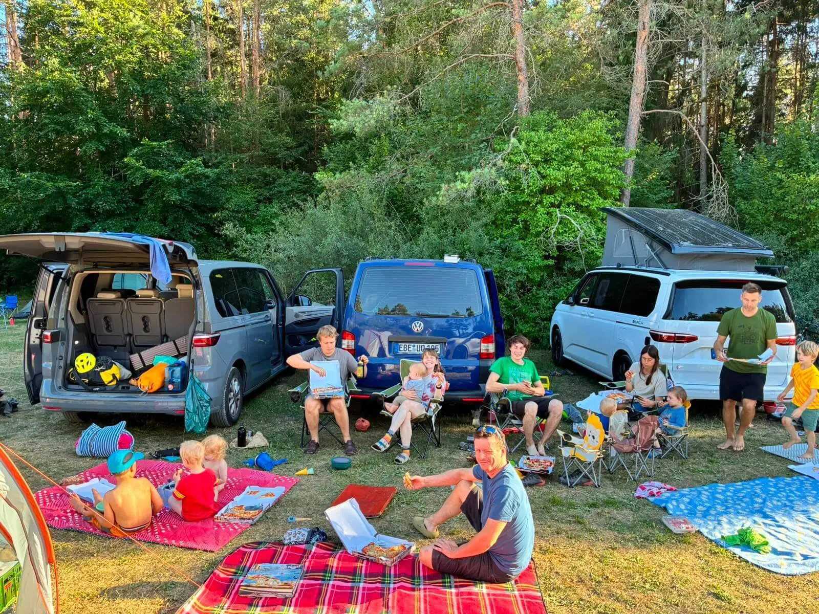 Familien sitzen auf Decken und Campingstühlen zwischen Fahrzeugen und Zelten. Auf dem Platz wird gemeinsam gegessen und pausiert. | © DAV Markt Schwaben/Lara Wolff