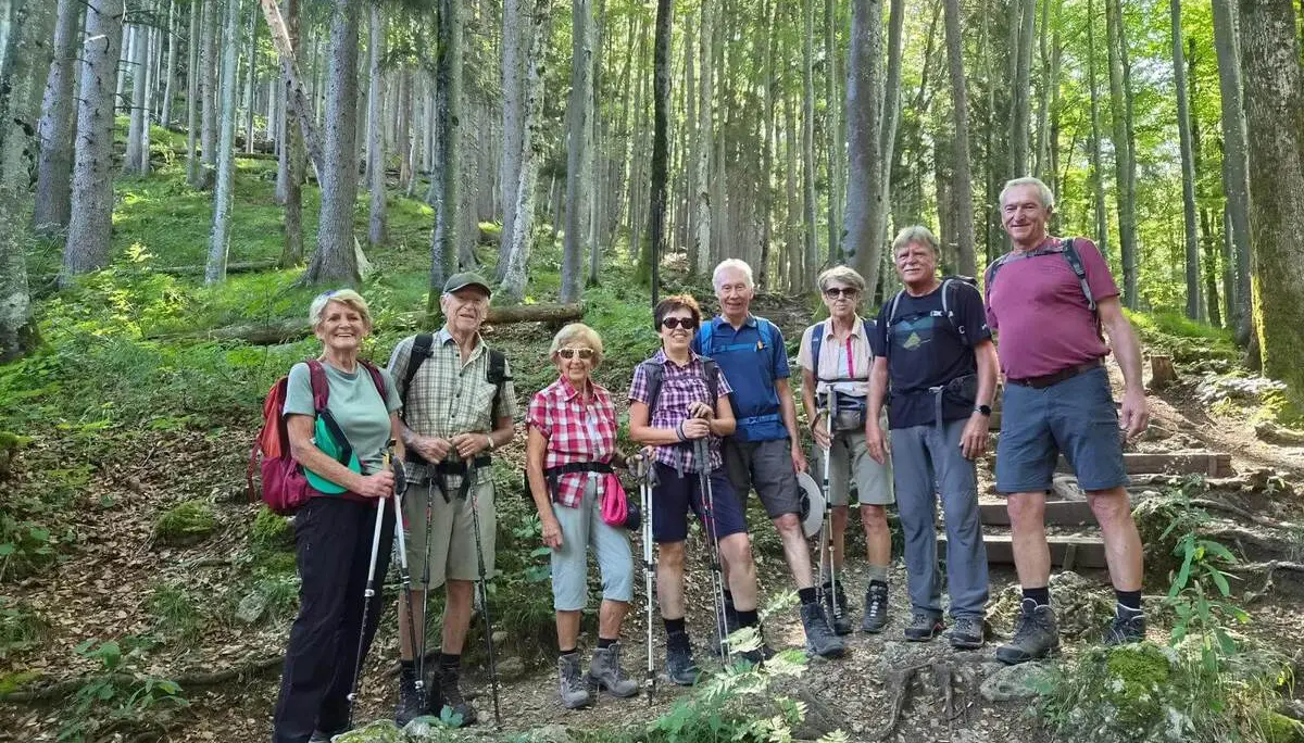 Acht Wandernde mit Rucksäcken und Trekkingstöcken posieren auf einem Waldpfad zwischen hohen Bäumen am Aufstieg zum Riederstein. | © DAV Markt Schwaben/Hubert Inhofer