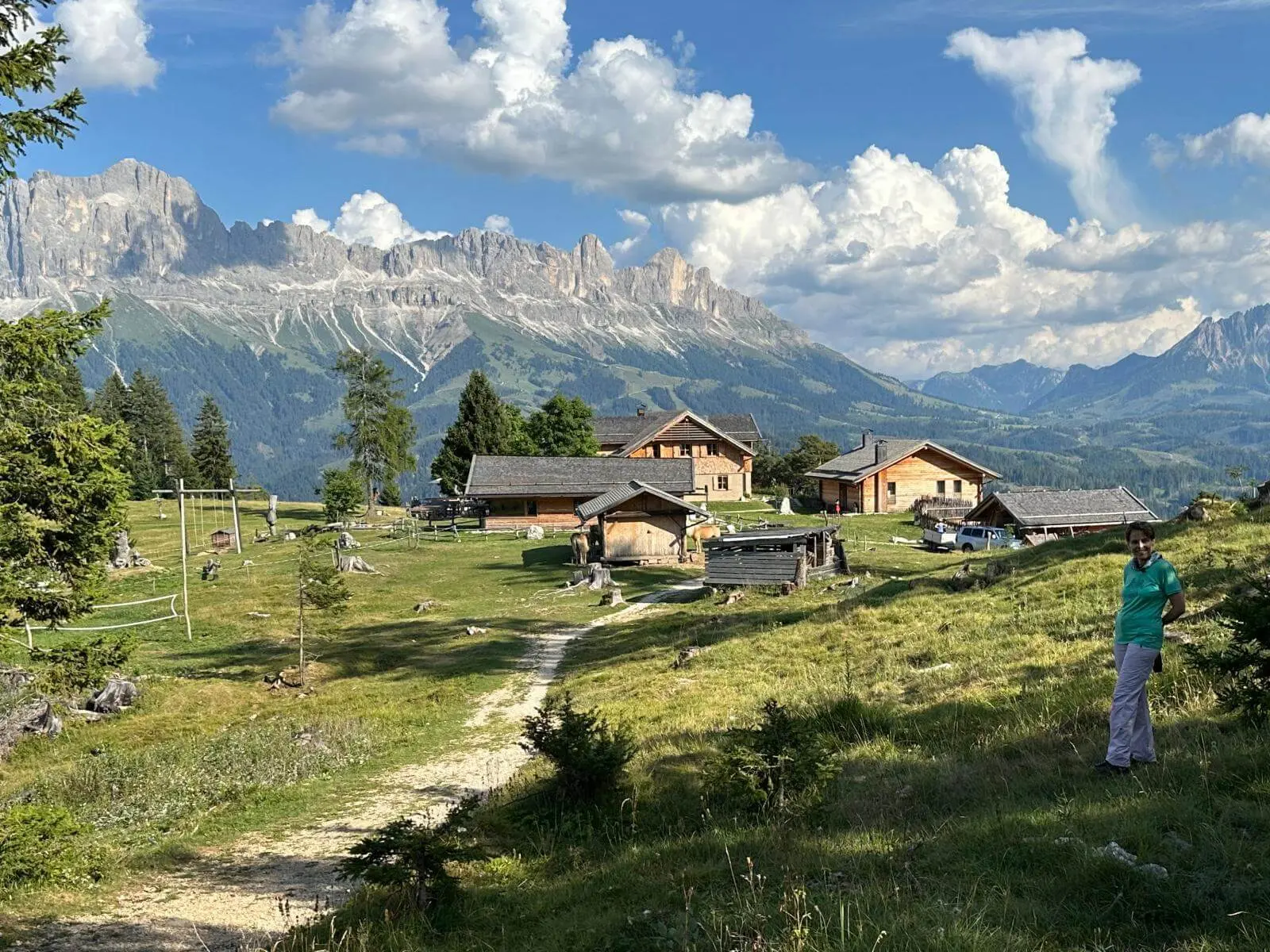 Almgelände mit Tschafon-Hütte und Nebengebäuden vor den Felswänden des Rosengartens; ein Weg führt über die Bergwiese. | © DAV Markt Schwaben/Christa Groß