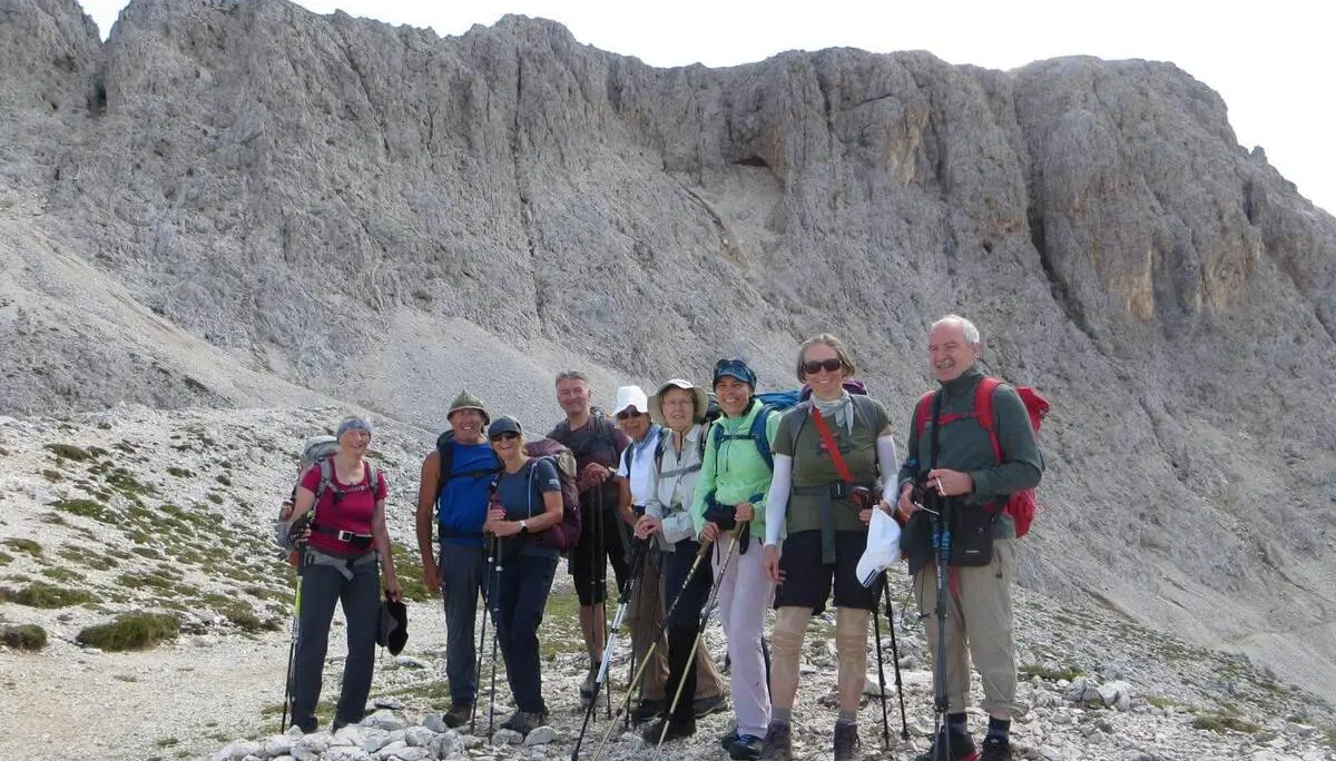 Wandergruppe mit Trekkingstöcken steht auf einem steinigen Pfad unter einer mächtigen Felswand im Rosengartengebiet. | © DAV Markt Schwaben/Gerlinde Hübl