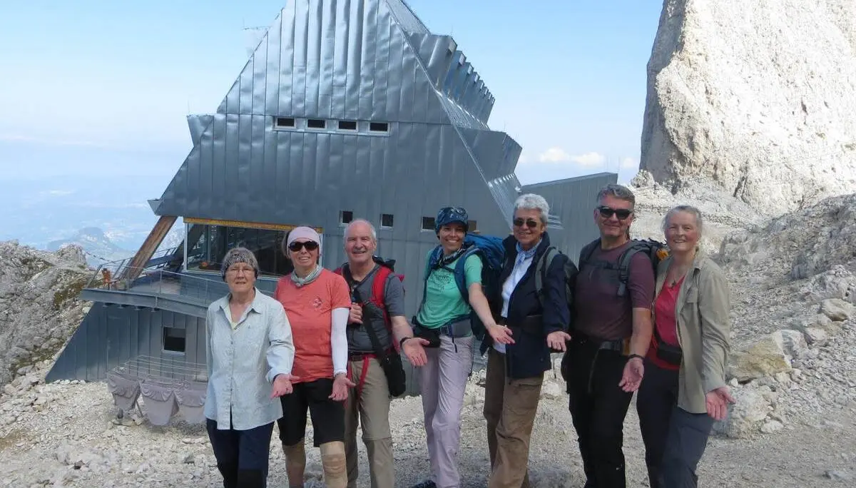 Wandergruppe steht vor der markanten Santnerpasshütte im felsigen Hochgebirge; dahinter ragen helle Dolomitwände empor. | © DAV Markt Schwaben/Gerlinde Hübl