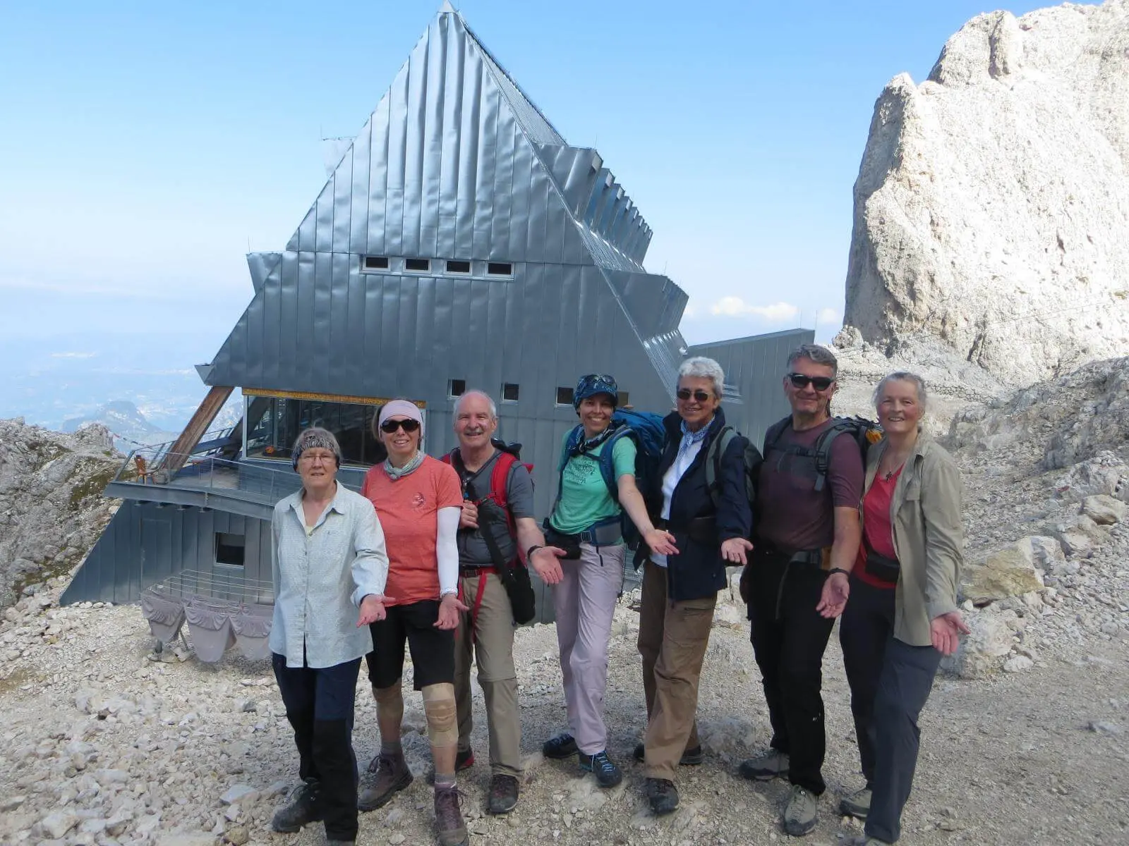 Wandergruppe steht vor der markanten Santnerpasshütte im felsigen Hochgebirge; dahinter ragen helle Dolomitwände empor. | © DAV Markt Schwaben/Gerlinde Hübl