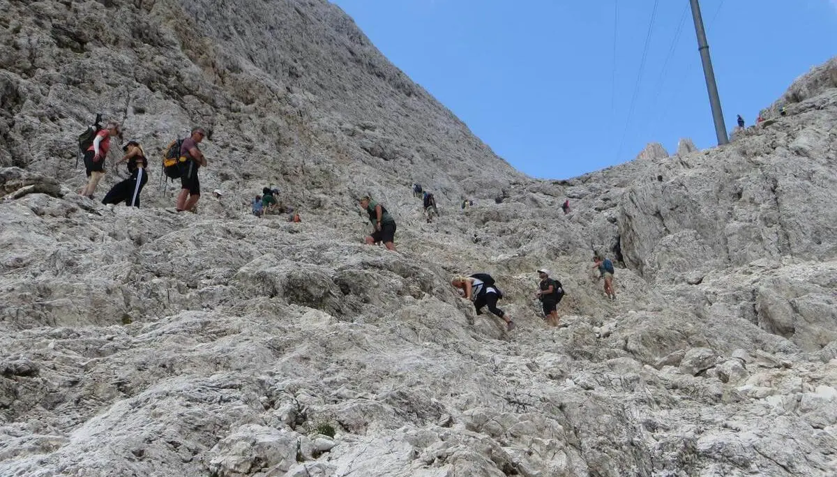 Zahlreiche Bergwandernde steigen durch steiles, felsiges Gelände zum Santnerpass auf; der Weg führt über hellen Kalkfels. | © DAV Markt Schwaben/Gerlinde Hübl