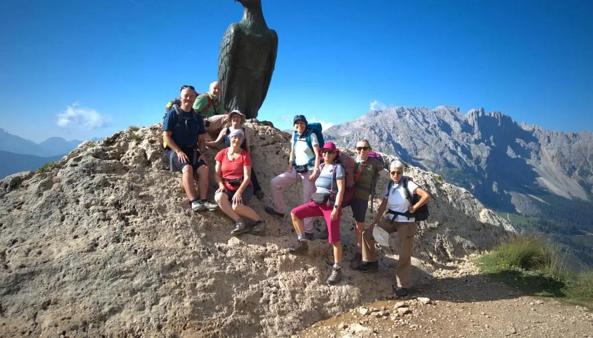 Wandergruppe posiert am Christomannos-Denkmal mit großem Bronzeadler; im Hintergrund erheben sich die Dolomiten. | © DAV Markt Schwaben/Markus Hübl