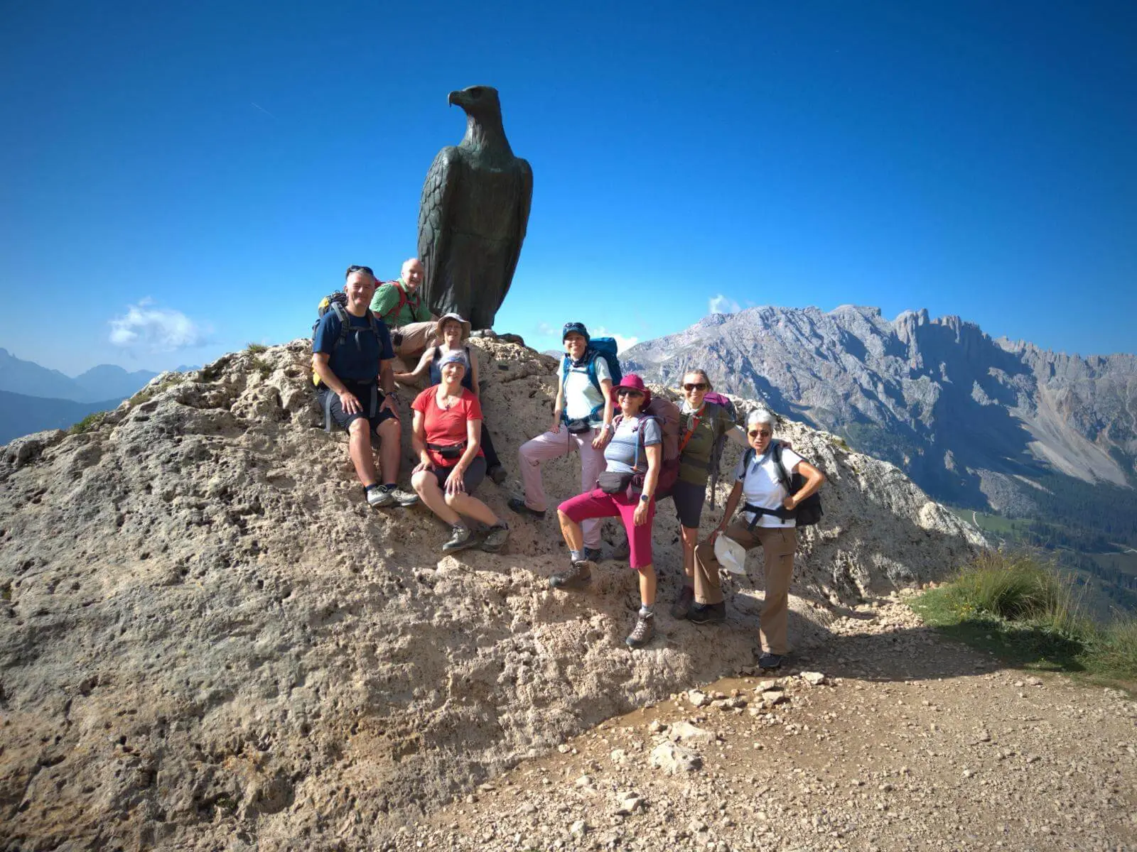 Wandergruppe posiert am Christomannos-Denkmal mit großem Bronzeadler; im Hintergrund erheben sich die Dolomiten. | © DAV Markt Schwaben/Markus Hübl