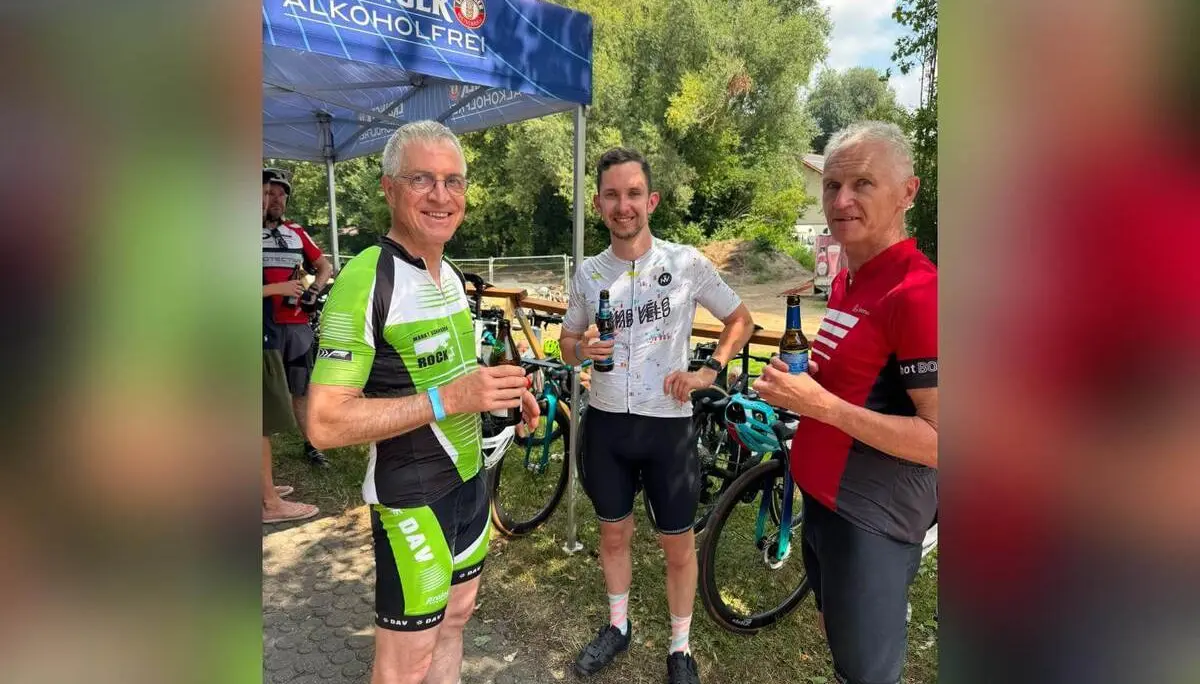 Drei Teilnehmende der Radtour stehen mit Getränken neben ihren Rennrädern unter einem Erdinger-Alkoholfrei-Zelt im Freien. | © DAV Markt Schwaben/Radsportgruppe