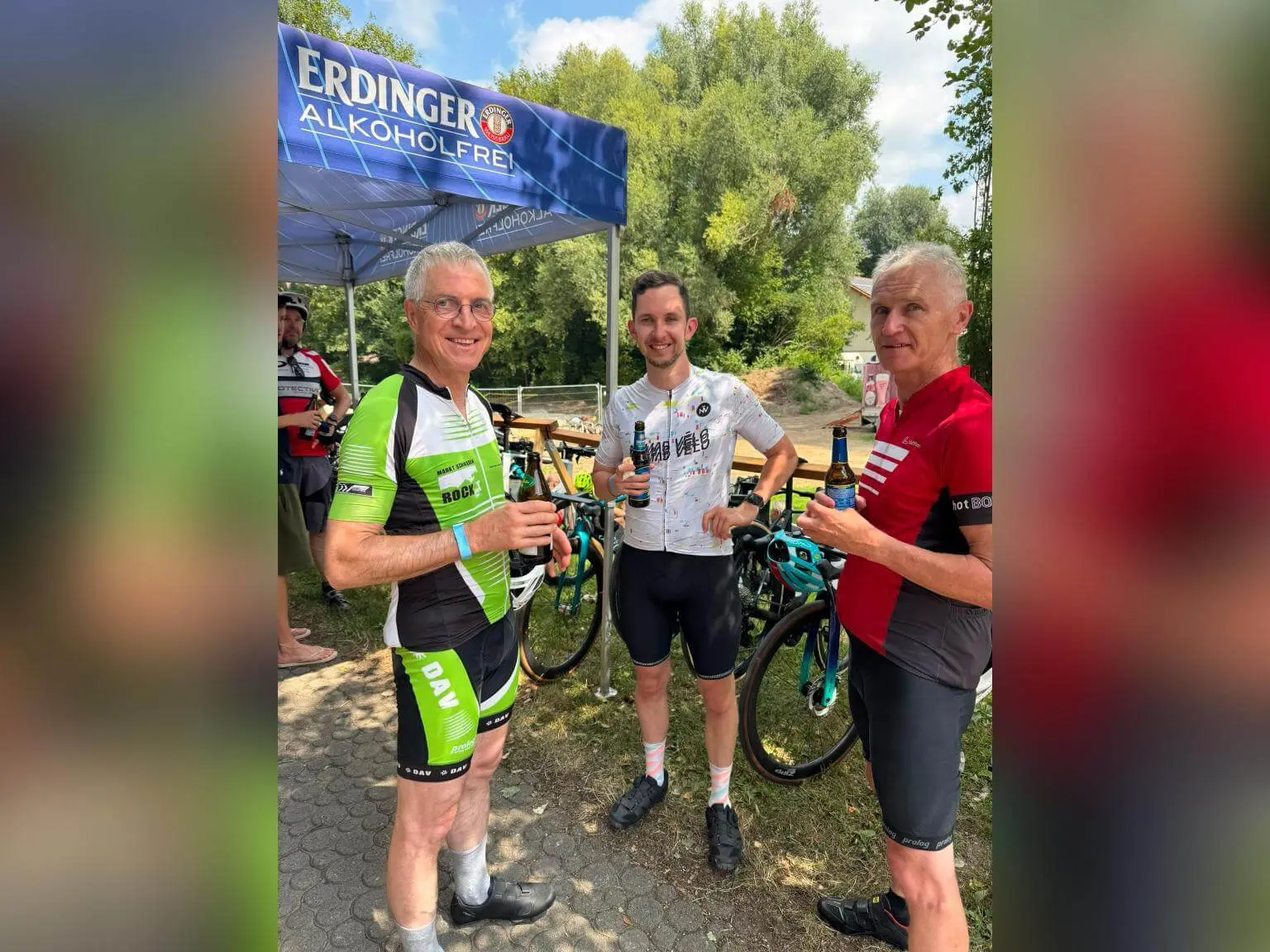 Drei Teilnehmende der Radtour stehen mit Getränken neben ihren Rennrädern unter einem Erdinger-Alkoholfrei-Zelt im Freien. | © DAV Markt Schwaben/Radsportgruppe