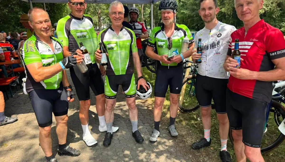 Sechs Teilnehmende der RTF stehen mit Getränken unter einem Erdinger-Alkoholfrei-Zelt. Im Hintergrund sind weitere Radfahrende und Rennräder zu sehen. | © DAV Markt Schwaben/Radsportgruppe