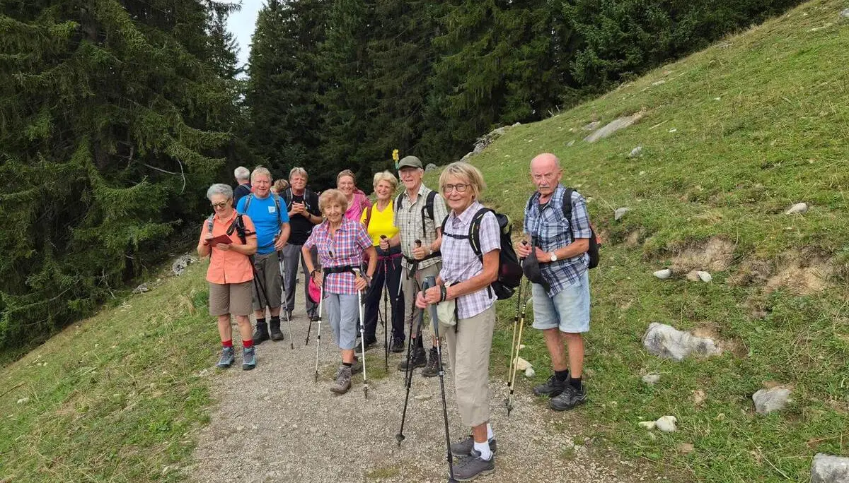 Die Wandergruppe steht mit Wanderstöcken auf einem breiten Schotterweg am Waldrand. Im Hintergrund steigen bewaldete Hänge an. | © DAV Markt Schwaben/Hubert Inhofer