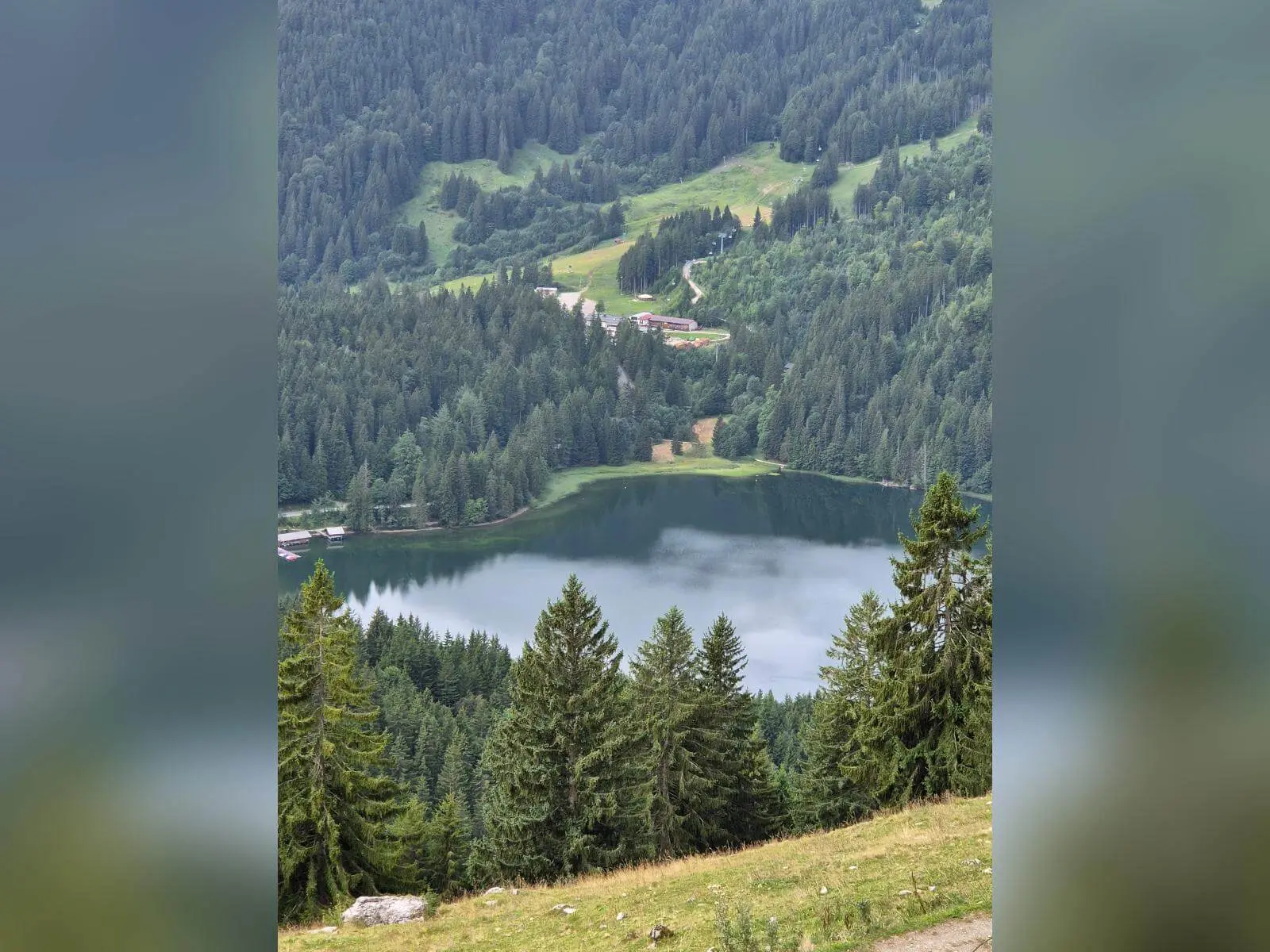 Blick von einem Berghang auf den Spitzingsee. Der See liegt zwischen dicht bewaldeten Hängen, einzelne Gebäude sind am Ufer zu erkennen. | © DAV Markt Schwaben/Hubert Inhofer