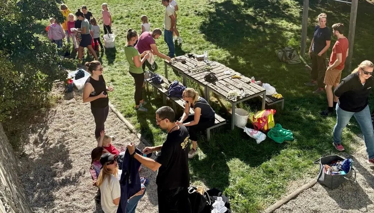 Familiengruppe bereitet auf einer Wiese Kleidung zum Batiken vor. Kinder und Erwachsene arbeiten gemeinsam an T-Shirts und Stoffen. | © DAV Markt Schwaben / Lara Wolff