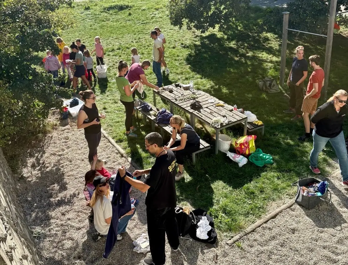 Familiengruppe bereitet auf einer Wiese Kleidung zum Batiken vor. Kinder und Erwachsene arbeiten gemeinsam an T-Shirts und Stoffen. | © DAV Markt Schwaben / Lara Wolff