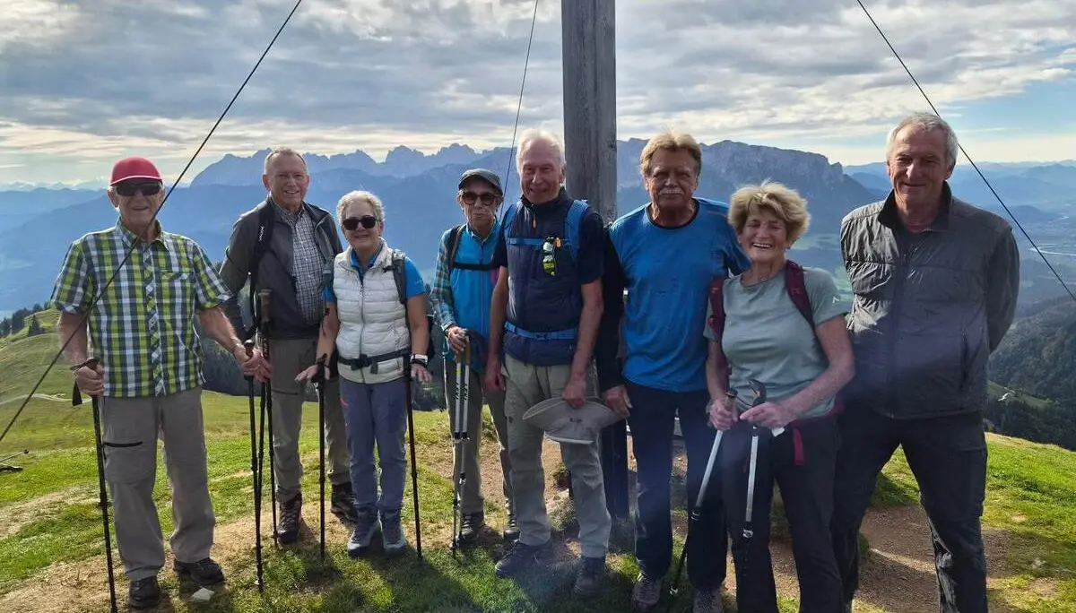 Wandergruppe mit Trekkingstöcken am Gipfelkreuz des Wandbergs; dahinter erstrecken sich Berge und Täler. | © DAV Markt Schwaben/Hubert Inhofer