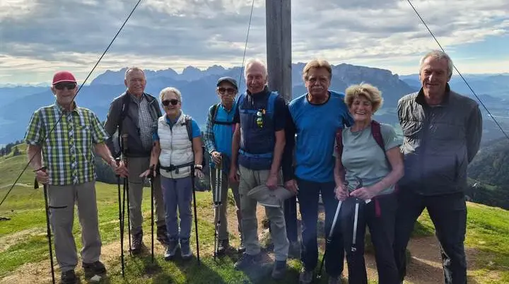 Wandergruppe mit Trekkingstöcken am Gipfelkreuz des Wandbergs; dahinter erstrecken sich Berge und Täler. | © DAV Markt Schwaben/Hubert Inhofer