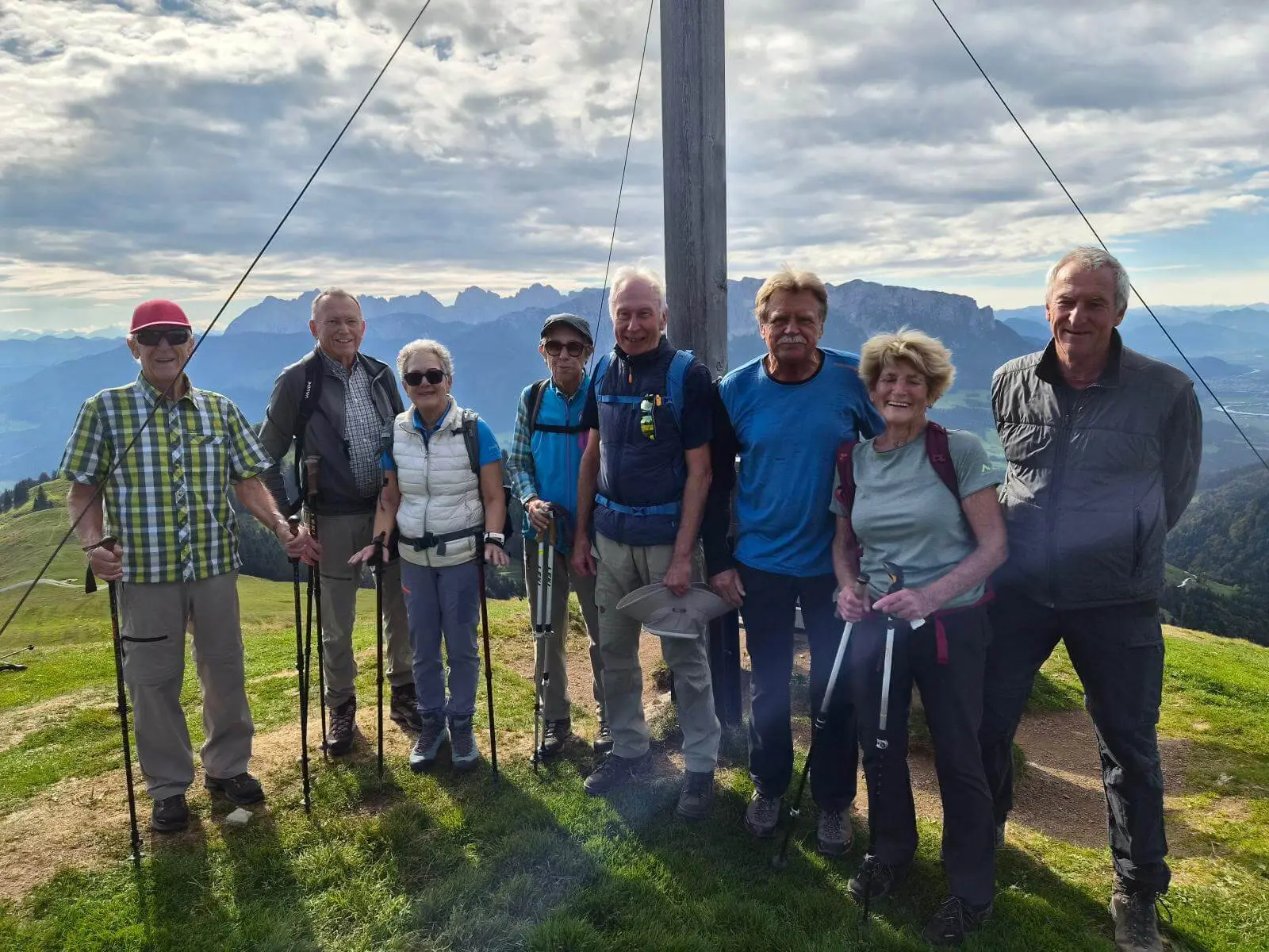 Wandergruppe mit Trekkingstöcken am Gipfelkreuz des Wandbergs; dahinter erstrecken sich Berge und Täler. | © DAV Markt Schwaben/Hubert Inhofer