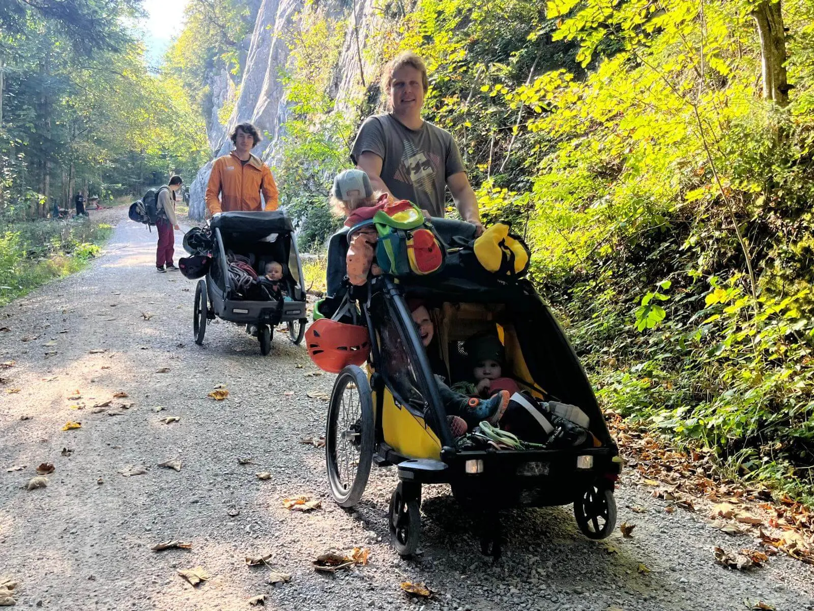 Familien mit Kindern sind auf einem breiten Waldweg zum Klettergarten unterwegs. Mehrere Kinder fahren in Anhängern mit. | © DAV Markt Schwaben/Lara Wolff