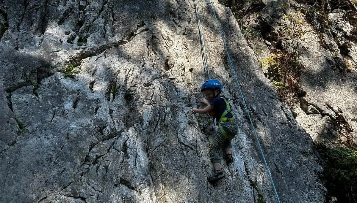 Ein Kind mit Kletterhelm und Gurt steigt an einer gesicherten Felswand empor. Das Seil verläuft oberhalb entlang der Route. | © DAV Markt Schwaben/Lara Wolff