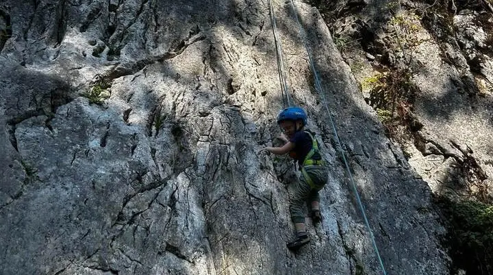 Ein Kind mit Kletterhelm und Gurt steigt an einer gesicherten Felswand empor. Das Seil verläuft oberhalb entlang der Route. | © DAV Markt Schwaben/Lara Wolff