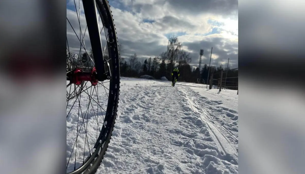 Nahaufnahme eines Fahrradreifens links im Vordergrund, dahinter fährt eine Person auf verschneitem Weg Richtung Horizont. | © DAV Markt Schwaben | Foto: Miron Thoms
