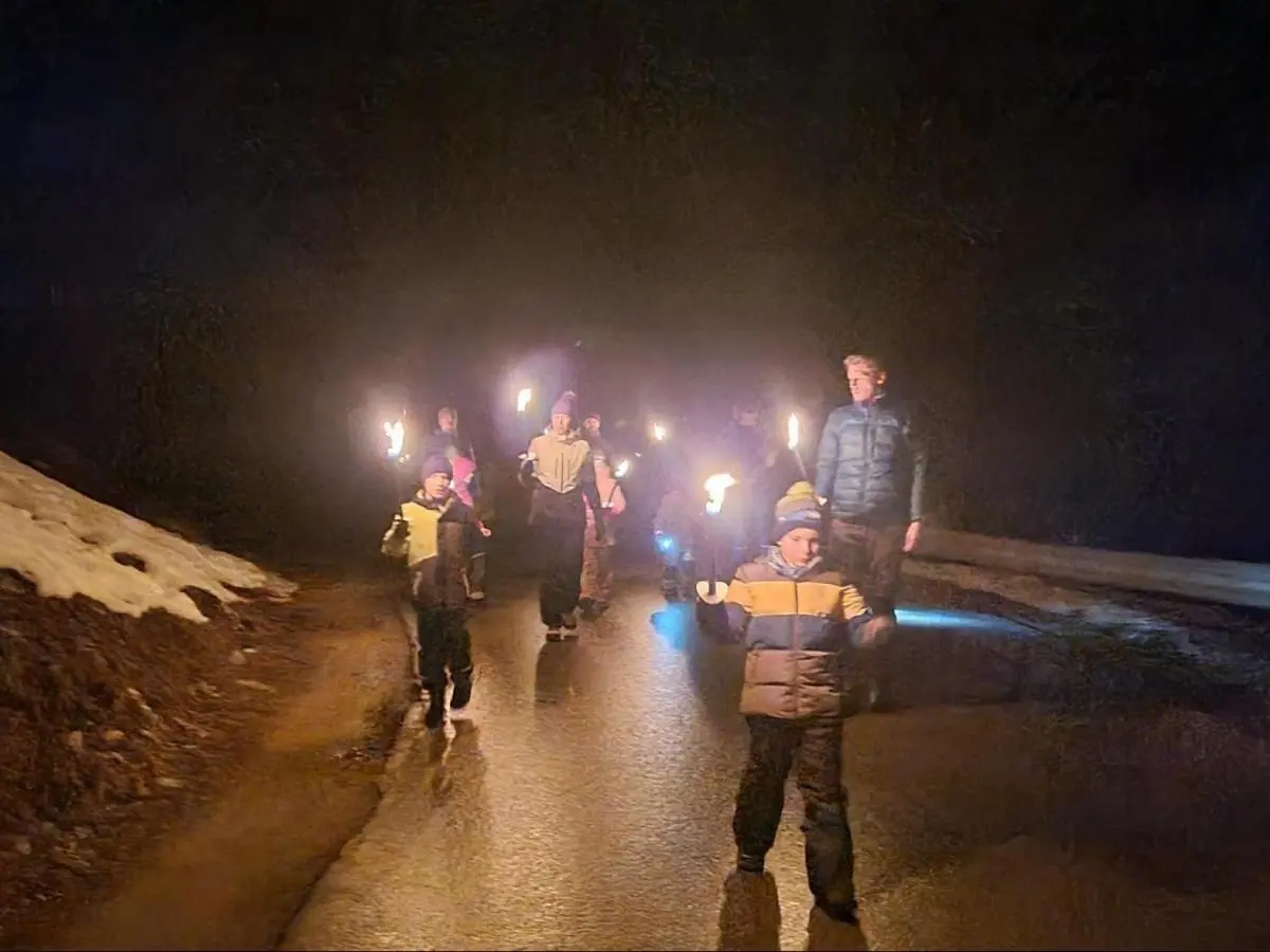 Kinder und Erwachsene gehen im Dunkeln mit brennenden Fackeln eine nasse Straße entlang; seitlich liegt Schnee, die Gruppe wirkt konzentriert und ruhig. | © DAV Markt Schwaben, Familiengruppe