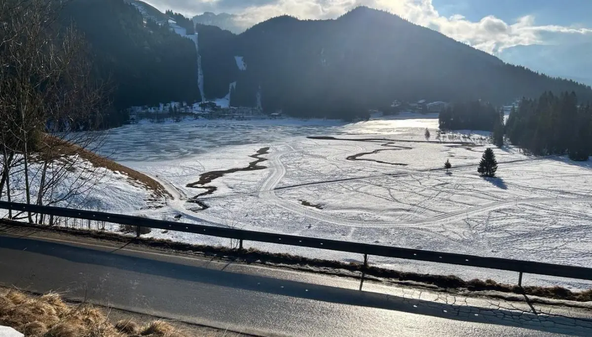 Sonnige Winterlandschaft mit gefrorenem See, verschneiten Hängen und Wald; Spuren im Schnee führen über die offene Fläche Richtung Berge. | © DAV Markt Schwaben, Familiengruppe