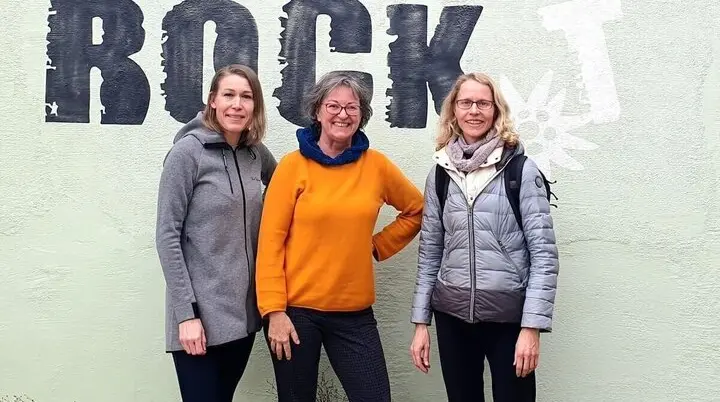 Drei Personen stehen vor einer Wand mit der Aufschrift „Markt Schwaben rockt“ und posieren gemeinsam als Team der Öffentlichkeitsarbeit. | © DAV Markt Schwaben / Anna Maria Blau