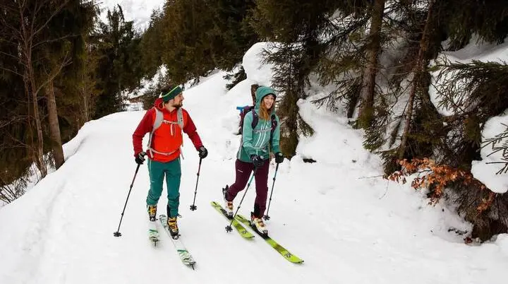 Zwei Personen steigen mit Tourenski durch verschneiten Wald bergauf; winterliche Szene als Teaser für Skitouren‑Ausrüstung. | © DAV / Marco Kost 2019