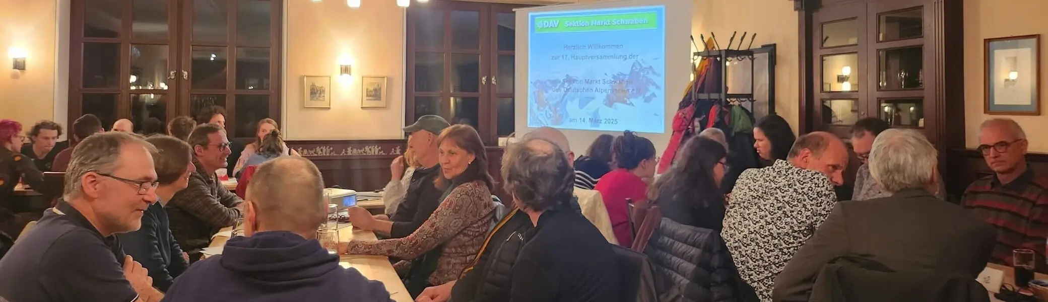 Mitglieder der DAV-Sektion Markt Schwaben sitzen an Tischen in einem Tagungsraum und verfolgen eine Präsentation während der jährlichen Mitgliederversammlung.“ | © DAV Markt Schwaben | Foto Anna Thoms