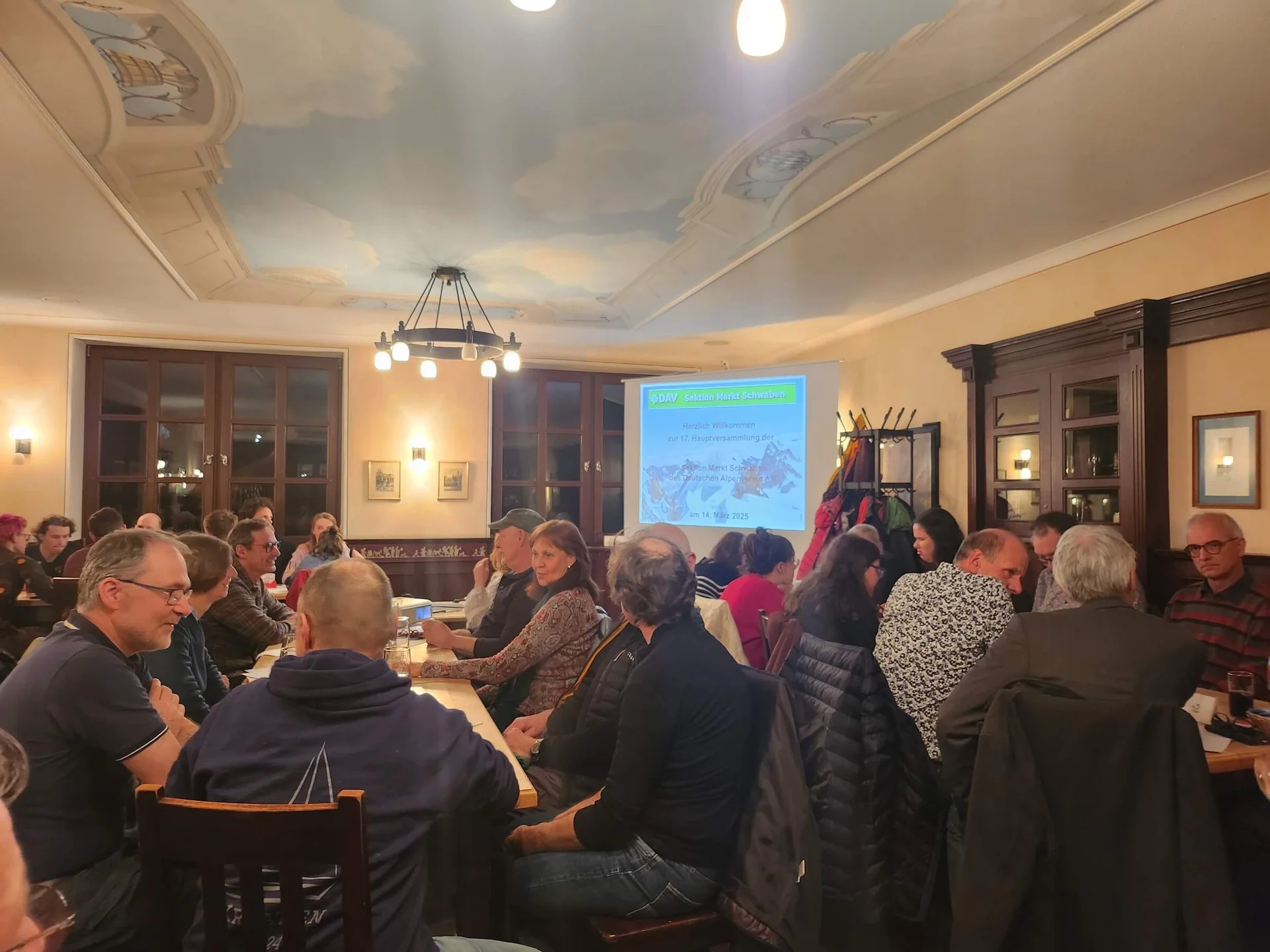 Mitglieder der DAV-Sektion Markt Schwaben sitzen an Tischen in einem Tagungsraum und verfolgen eine Präsentation während der jährlichen Mitgliederversammlung.“ | © DAV Markt Schwaben | Foto Anna Thoms
