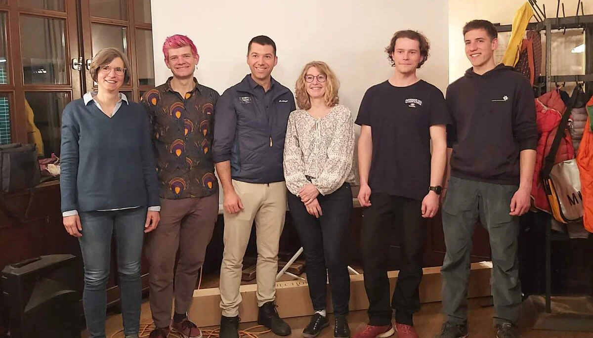 Sechs Personen, der neu gewählte Vorstand, stehen in einem Raum mit einer Leinwand und Holzfußboden. | © DAV Markt Schwaben | Foto Martina Straub