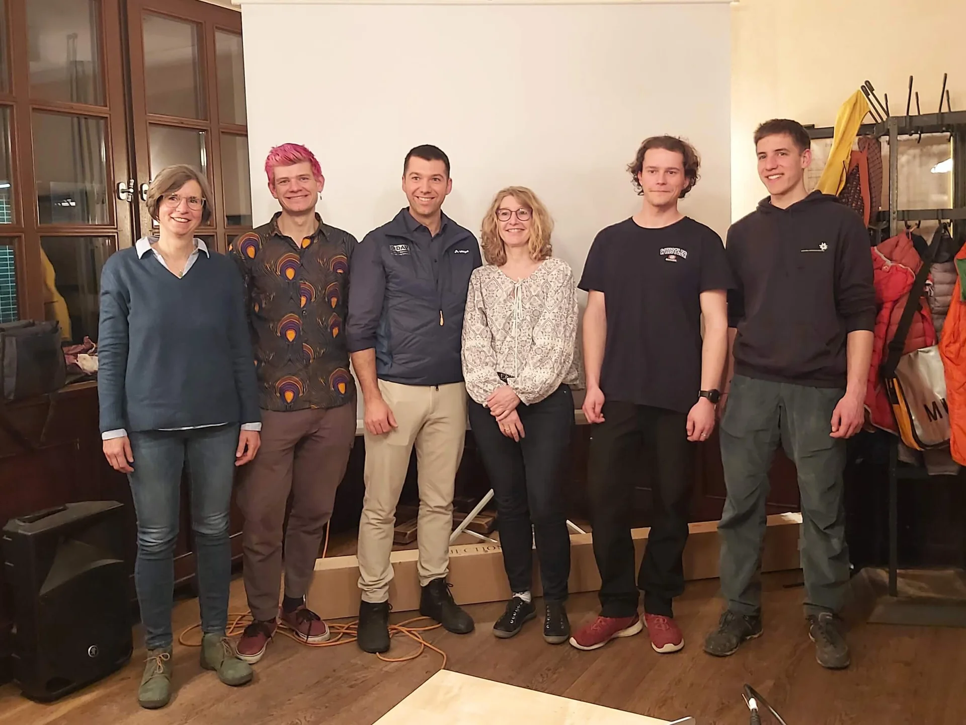 Sechs Personen, der neu gewählte Vorstand, stehen in einem Raum mit einer Leinwand und Holzfußboden. | © DAV Markt Schwaben | Foto Martina Straub