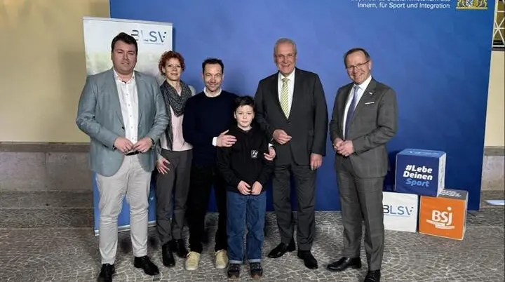 Sechs Personen stehen vor blauem Hintergrund mit Logos des bayerischen Innenministeriums und Sportverbänden; sie posieren für ein offizielles Foto. | © BLSV/​Hermann