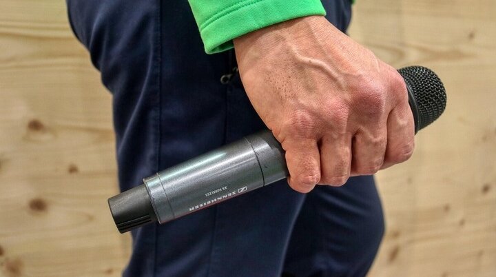 Eine Hand hält ein Sennheiser-Mikrofon während einer Veranstaltung. Die Person trägt grün und blau. | © Image by Alexander Fox | PlaNet Fox from Pixabay