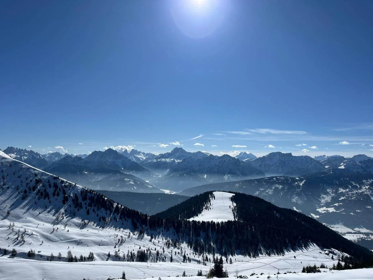 Sonnenbeschienener Dolomitenhang mit Skispuren und Blick auf bewaldeten Grat; im Hintergrund schroffe Gipfel und blauer Himmel. | © DAV Markt Schwaben · Foto: Peter Langenbacher