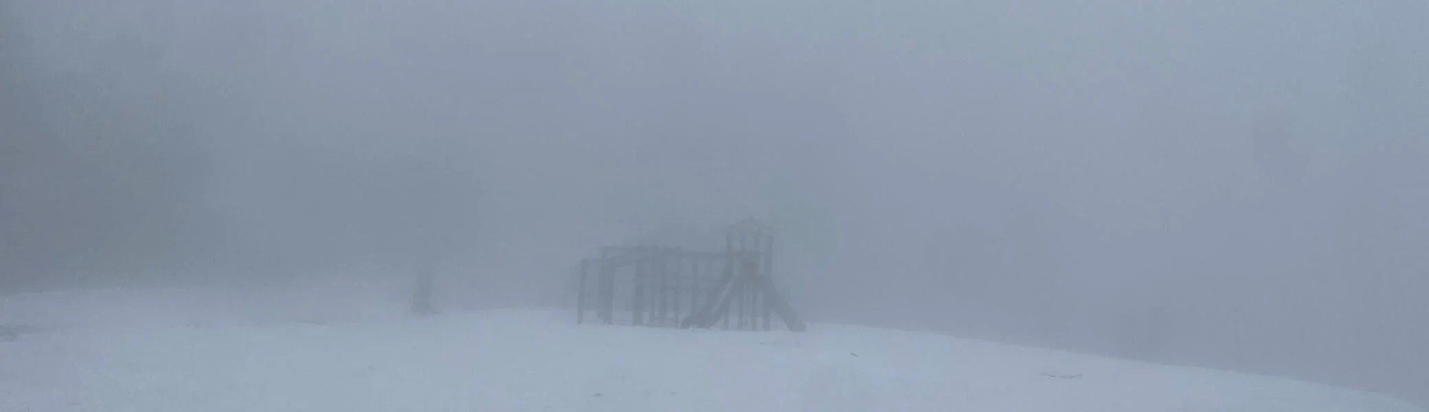 Spielplatzstruktur mit Rutsche und Kletterelementen, umgeben von Schnee und dichtem Nebel für eine mystische Atmosphäre. | © DAV Markt Schwaben