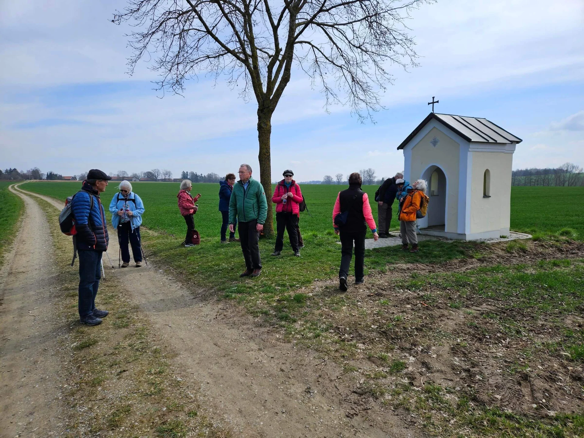 eniorengruppe auf einem sonnigen Feldweg, lachend und entspannt beim Wandern – neben einer kleinen Kapelle | © DAV Markt Schwaben